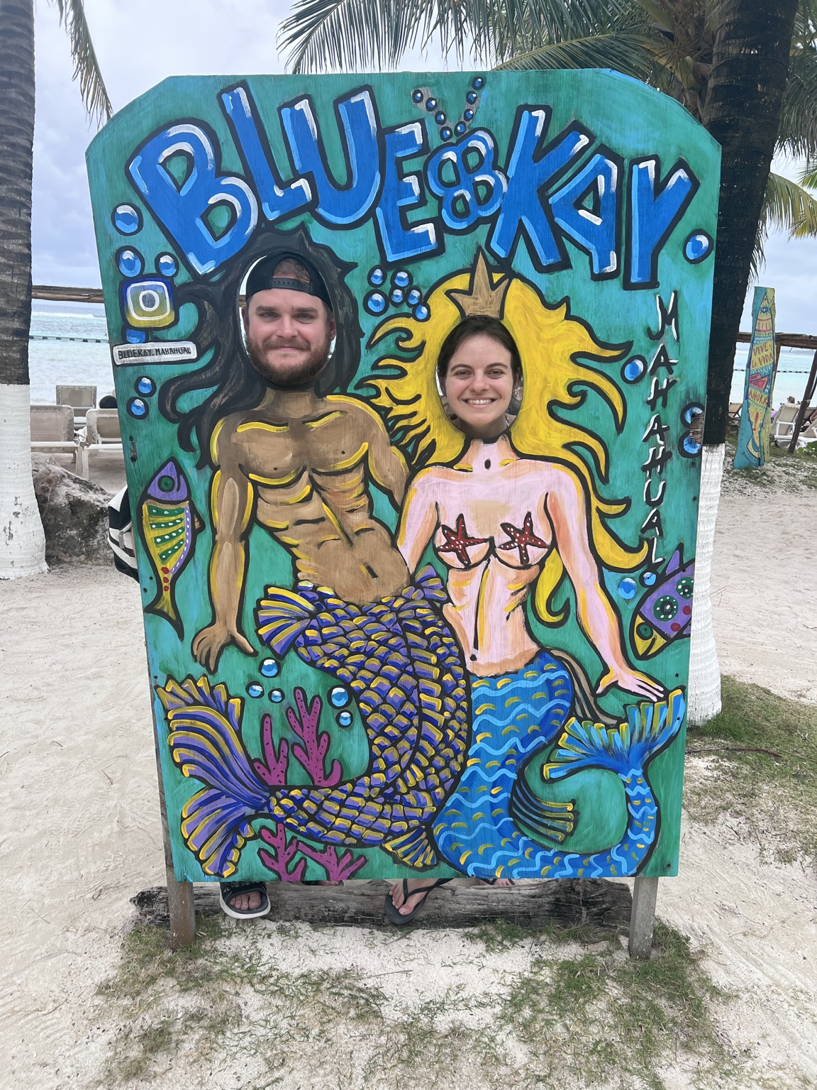 Paige and Charles posing in a goofy mermaid and merman beach cutout